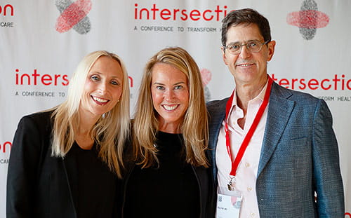 Three attendees pose in front of the Intersection banner