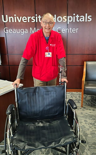 Guy, a volunteer at UH Geauga Medical Center, stands behind an empty wheelchair